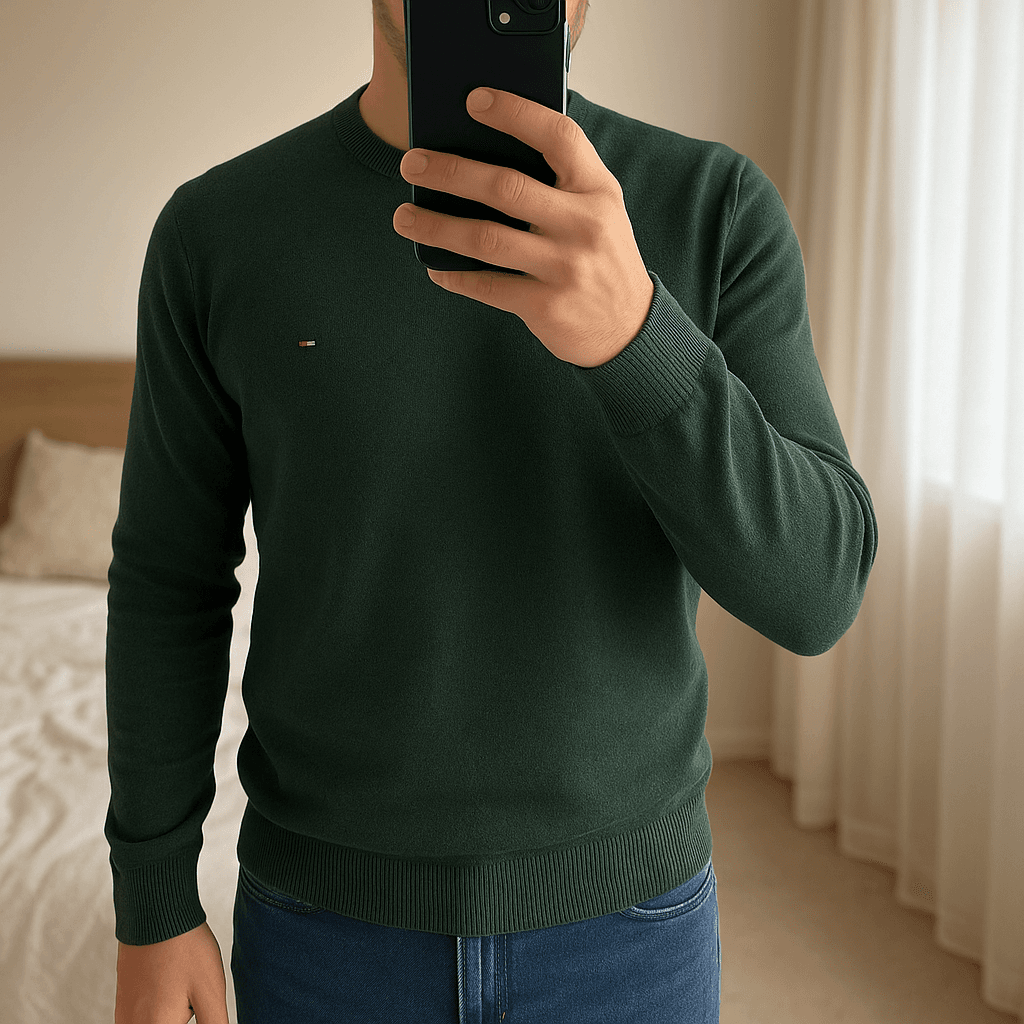 Pull Col Rond 100% Organic Coton Tommy Hilfiger Vert S debout, face à la caméra, dans une chambre à la lumière douce, avec une lumière naturelle filtrant par la fenêtre.