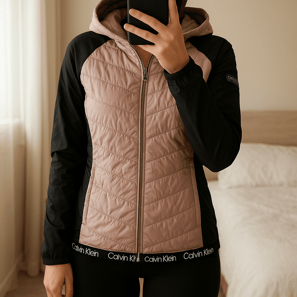 Calvin Klein pink women's jacket standing straight facing the camera, in a softly lit bedroom setting, with gentle natural light filtering through a window.