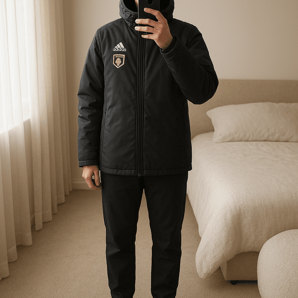 Casaco comprido adidas tamanho M mas veste grande em pé, de frente para a câmera, em um quarto com iluminação suave e luz natural filtrando pela janela.