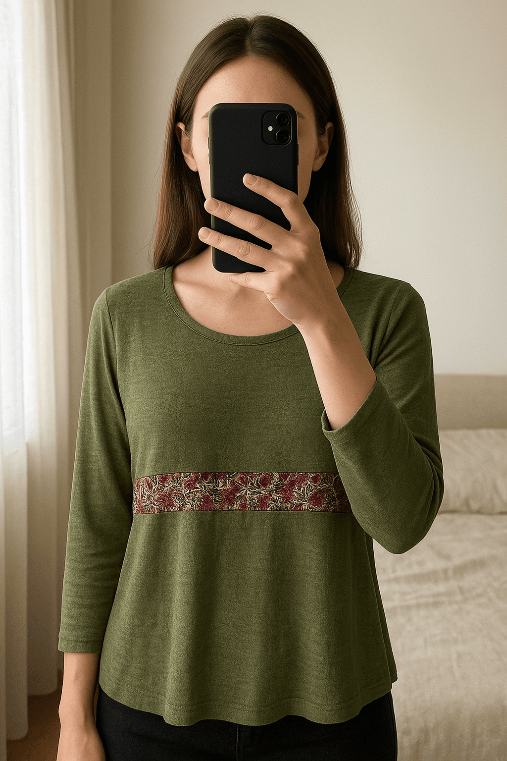 Camisola Natura em pé, de frente para a câmera, em um quarto com iluminação suave e luz natural filtrando pela janela.