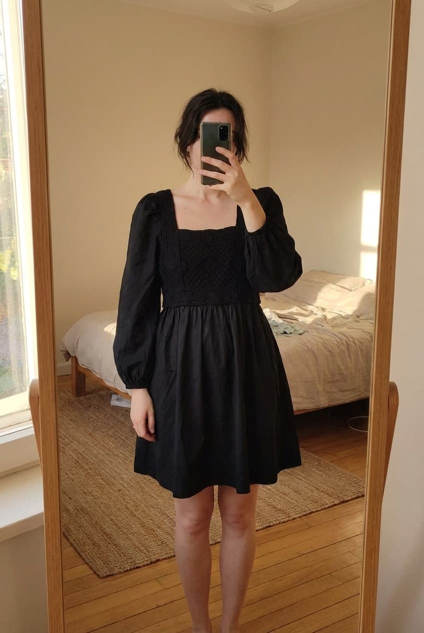 Robe courte manche bouffante bi matière debout, face à la caméra, dans une chambre à la lumière douce, avec une lumière naturelle filtrant par la fenêtre.