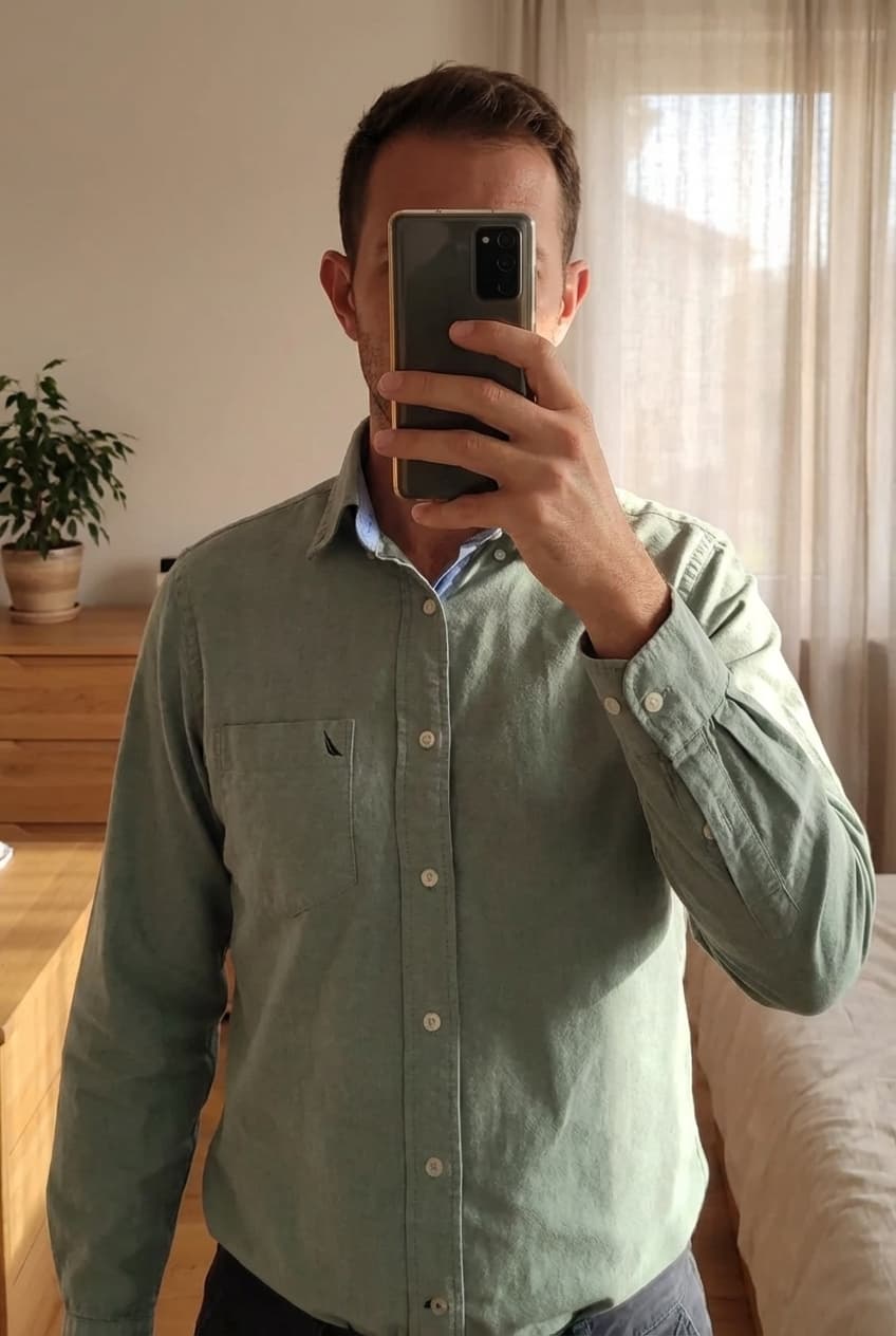 Une personne en Chemise manche longue, Nautica, taille S debout, face à la caméra, dans une chambre à la lumière douce, avec une lumière naturelle filtrant par la fenêtre.