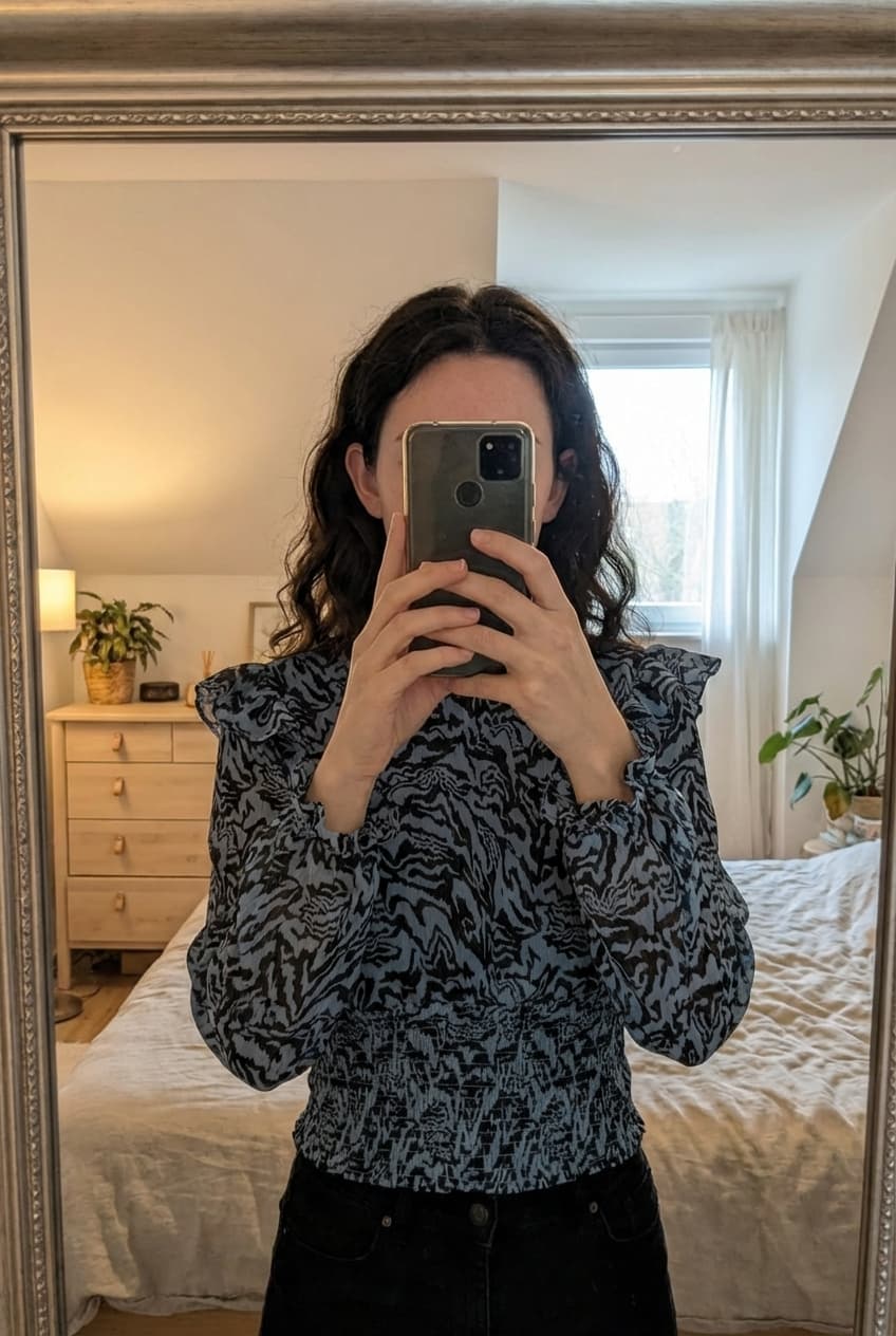 Chemisier à motifs debout, face à la caméra, dans une chambre à la lumière douce, avec une lumière naturelle filtrant par la fenêtre.