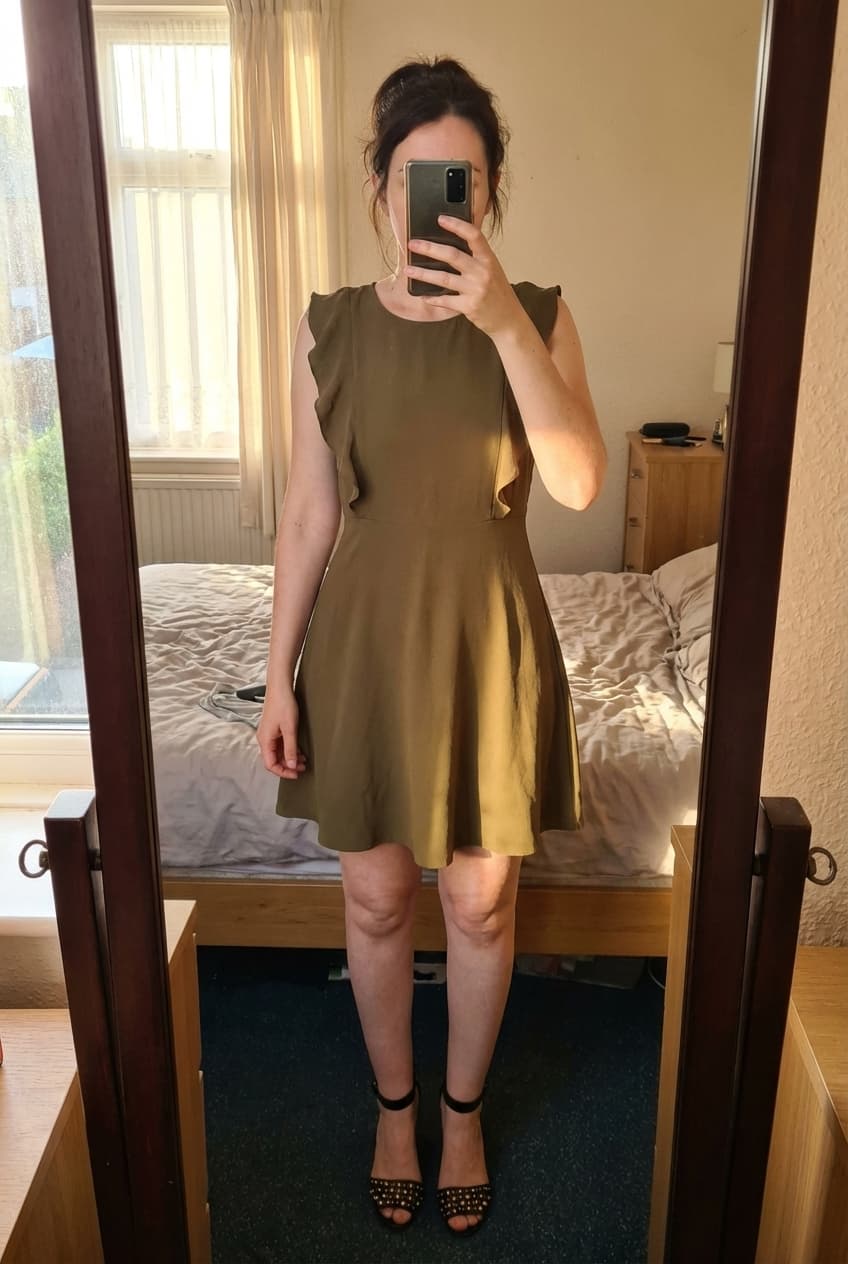 Très jolie robe taille 36 debout, face à la caméra, dans une chambre à la lumière douce, avec une lumière naturelle filtrant par la fenêtre.