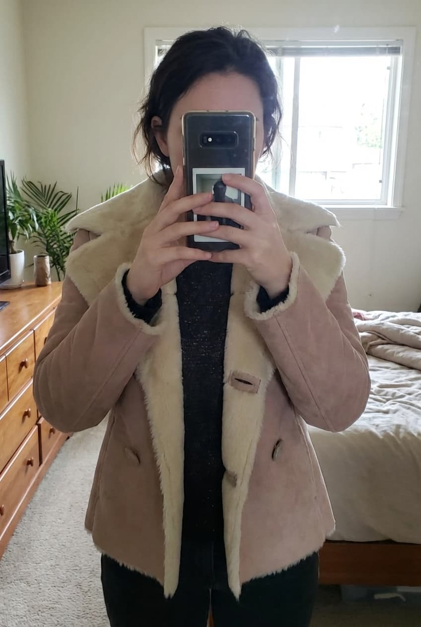 Veste d'hivers debout, face à la caméra, dans une chambre à la lumière douce, avec une lumière naturelle filtrant par la fenêtre.