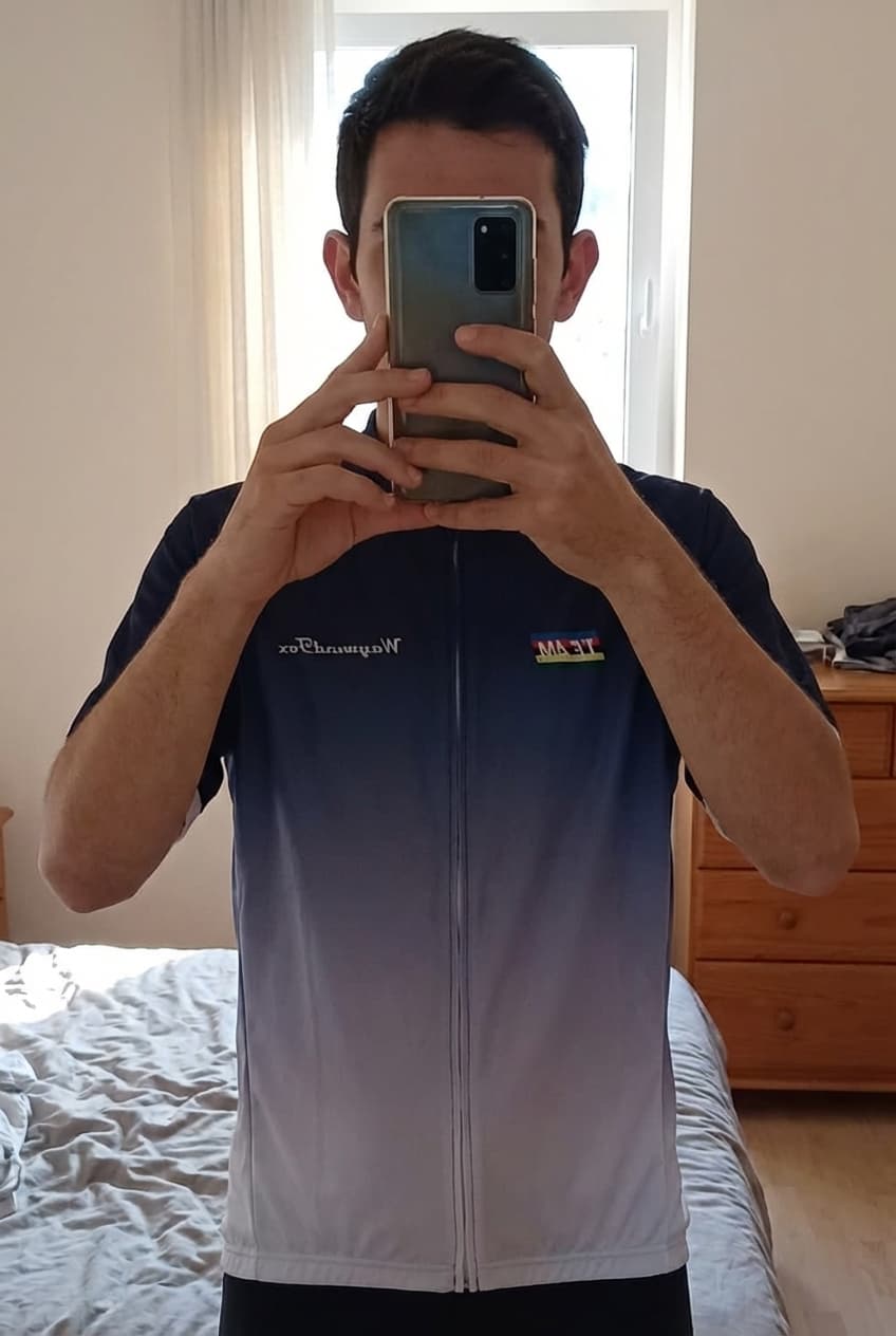 Maillot de cyclisme / XXXL debout, face à la caméra, dans une chambre à la lumière douce, avec une lumière naturelle filtrant par la fenêtre.